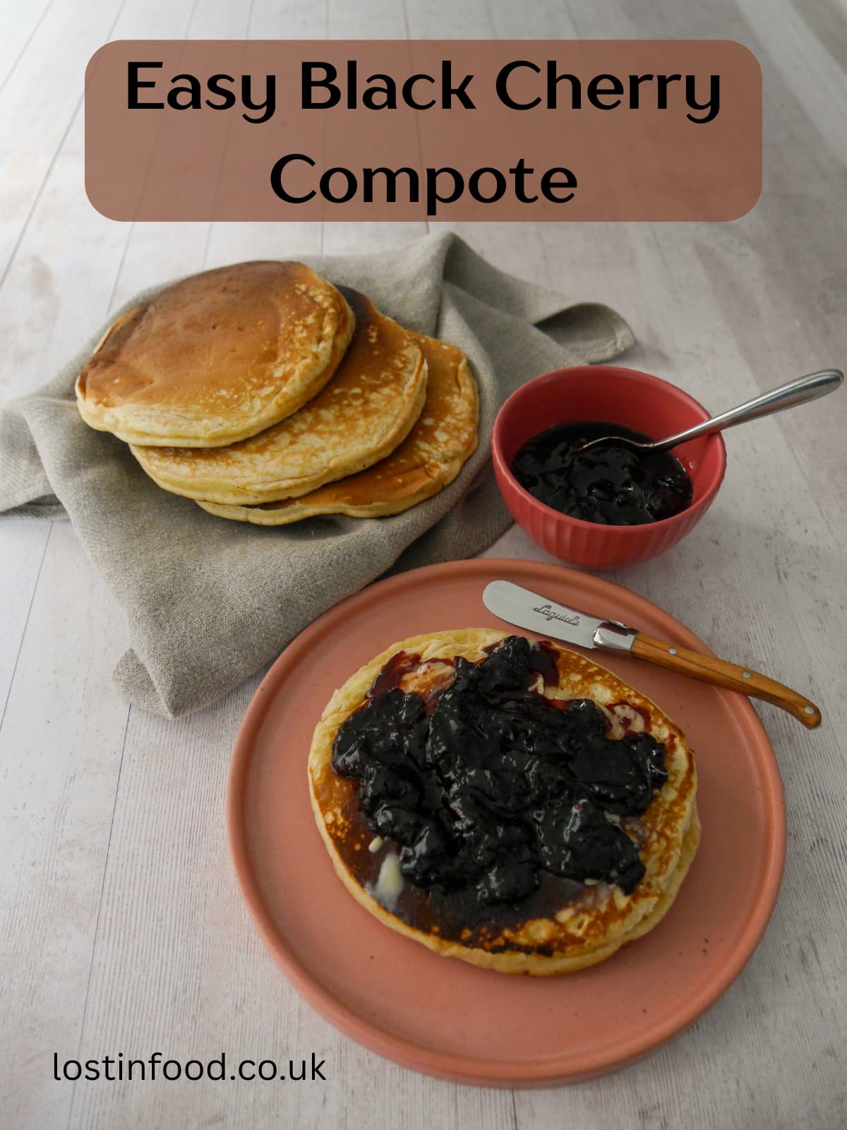 Pinnable image with recipe title and a plate with a pancake topped with black cherry compote, with a bowl of compote and some extra pancakes set alongside.