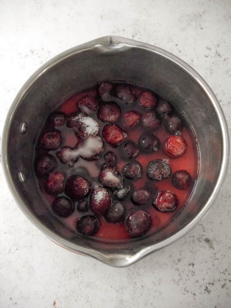 A saucepan of black cherries with added water and sugar.