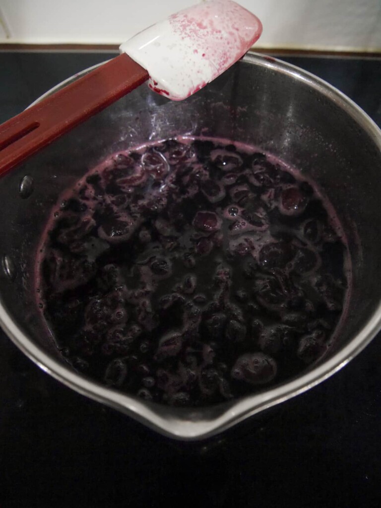 A saucepan of cooked black cherries, sugar and water.