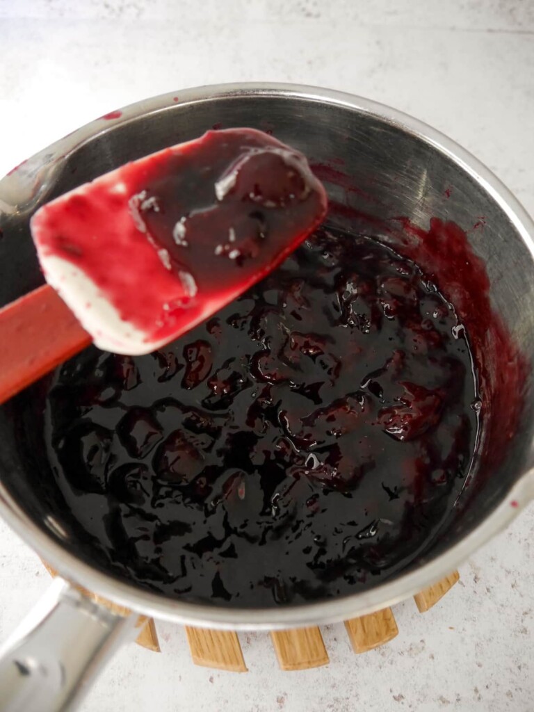 A saucepan of cooked and thickened black cherry compote.
