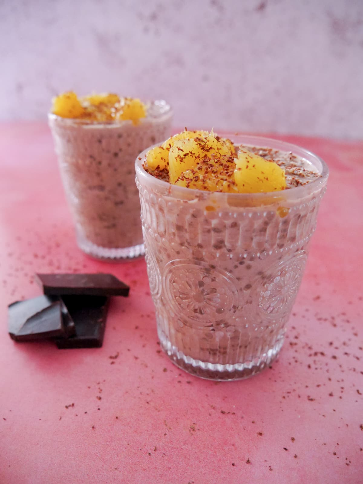 Two glasses filled with chocolate orange overnight oats, topped with orange segments and grated dark chocolate.