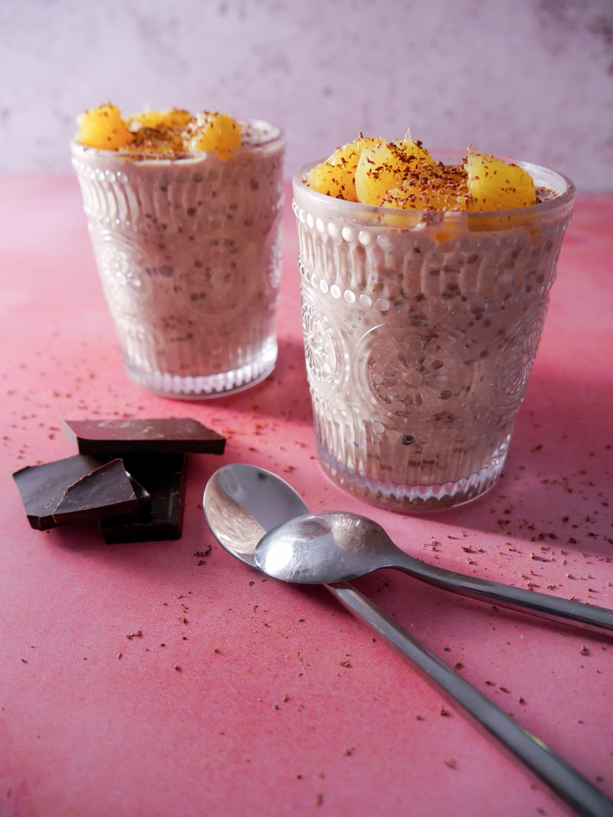 Two glasses filled with chocolate orange overnight oats, topped with orange segments and grated dark chocolate.