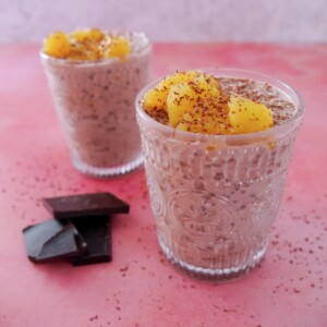 Two glasses filled with chocolate orange overnight oats, topped with orange segments and grated dark chocolate.