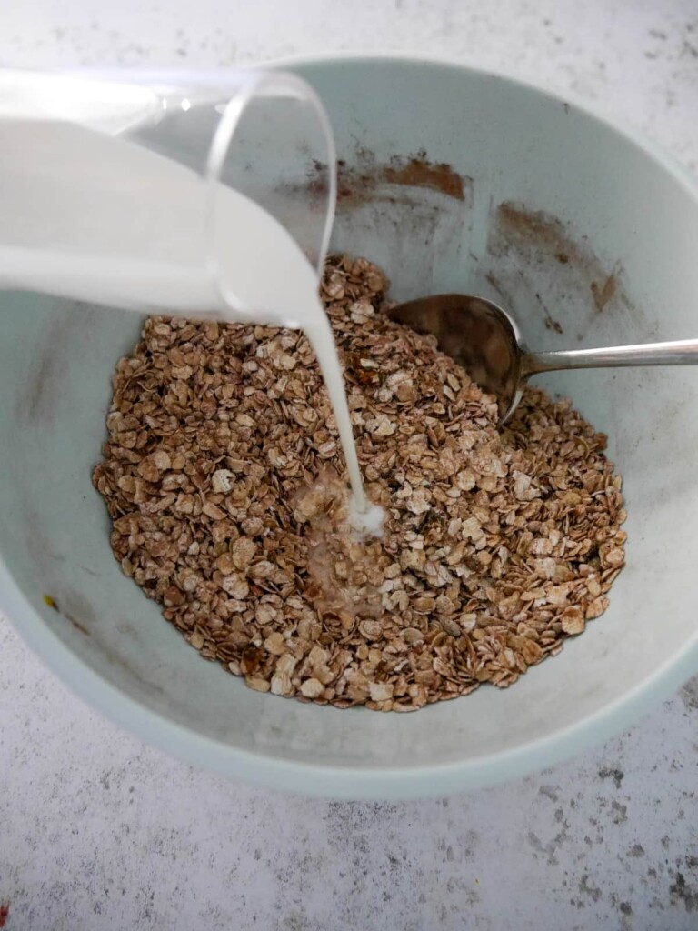 A bowl of porridge oats (rolled oats) with added cocoa powder, grated orange zest and chia seeds, with whole milk being poured over.