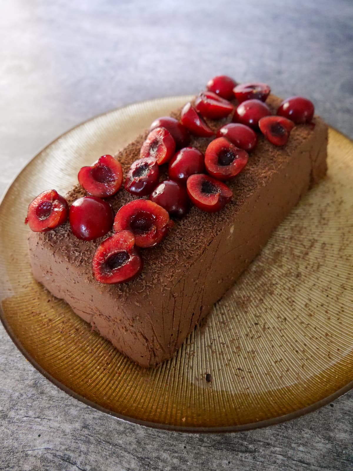 A gold plate topped with frozen dark chocolate parfait, topped with halved fresh cherries and grated 85% dark chocolate.