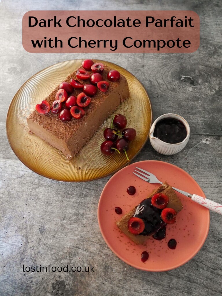 Pinnable image with recipe title and a gold plate topped with frozen dark chocolate parfait, and a plate with a slice of chocolate parfait topped with fresh cherries and cherry compote, and a jug of cherry compote set alongside.