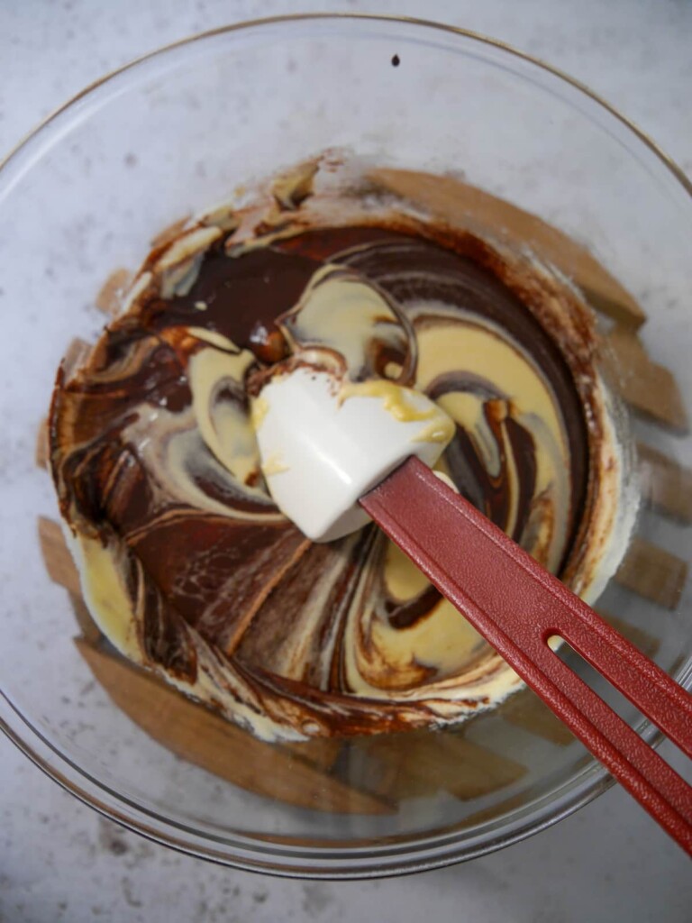 Whipped egg yolks and sugar being added to a bowl of melted dark chocolate.
