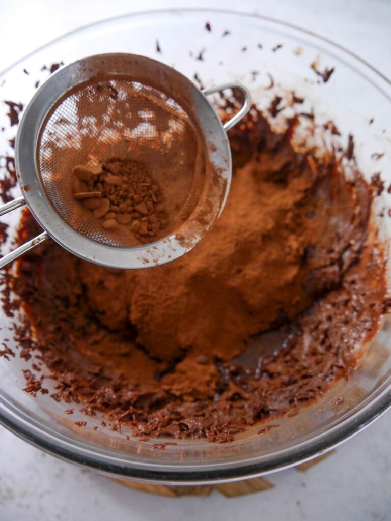 A bowl of combined melted dark chocolate, whipped egg whites and sugar, with cocoa powder being added.