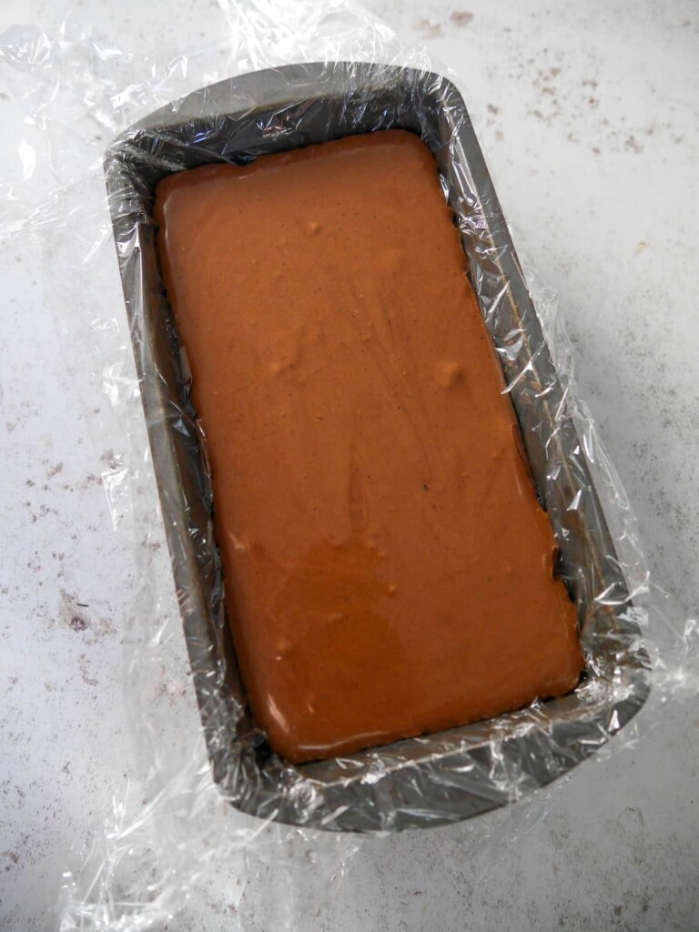 A loaf tin lined with clingfilm and filled with chocolate parfait mixture.