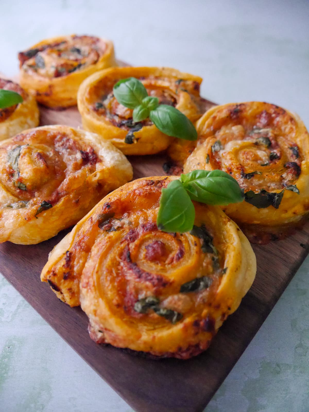 A wooden board topped with red pesto pinwheels garnished with basil leaves.