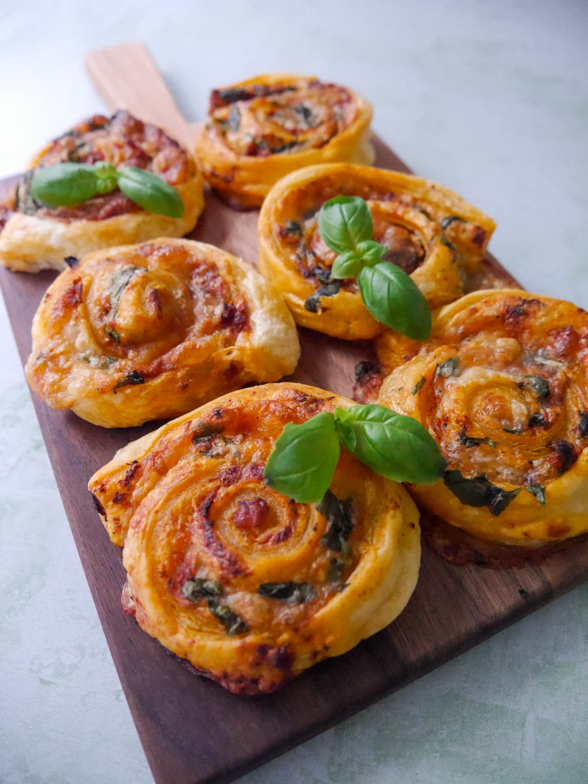 A wooden board topped with red pesto pinwheels garnished with basil leaves.