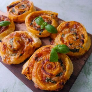 A wooden board topped with red pesto pinwheels garnished with basil leaves.