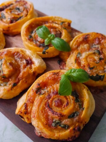 A wooden board topped with red pesto pinwheels garnished with basil leaves.