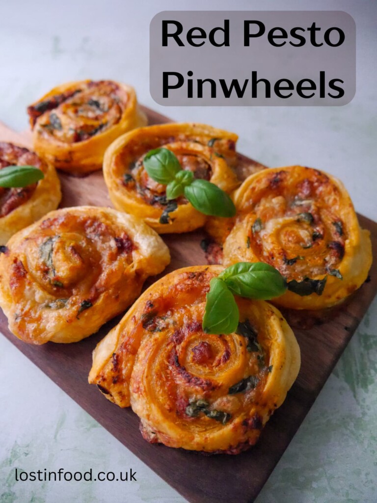 Pinnable image with recipe title and a wooden board topped with red pesto pinwheels garnished with basil leaves.