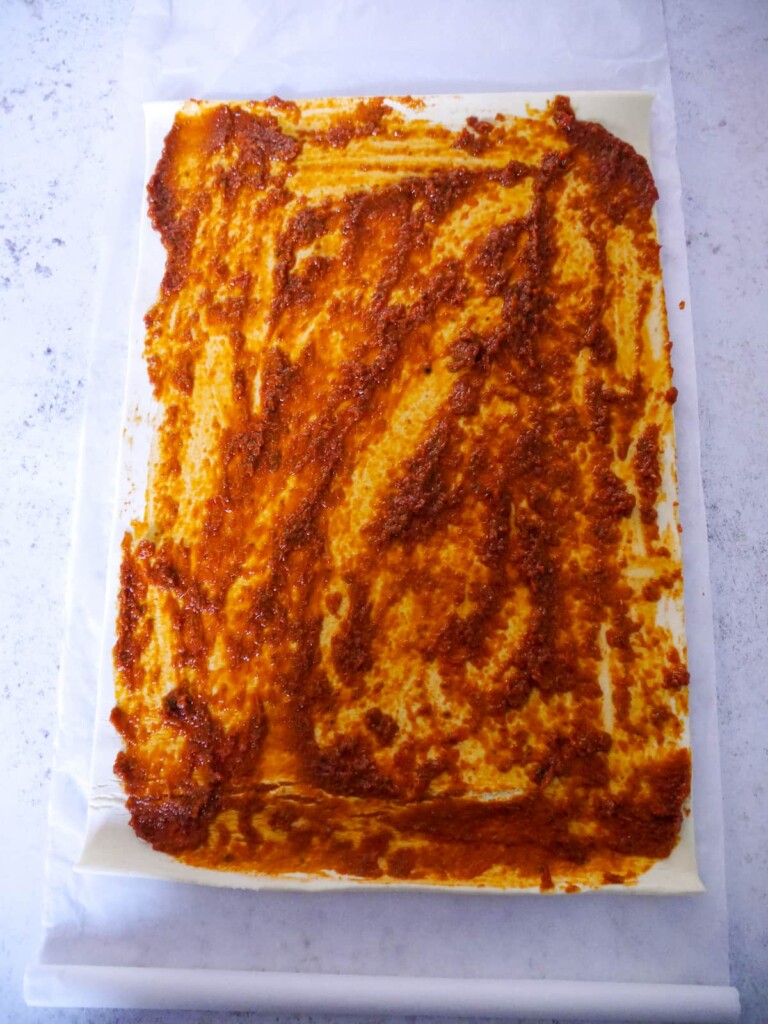 A sheet of puff pastry spread with a thin layer of red pesto.