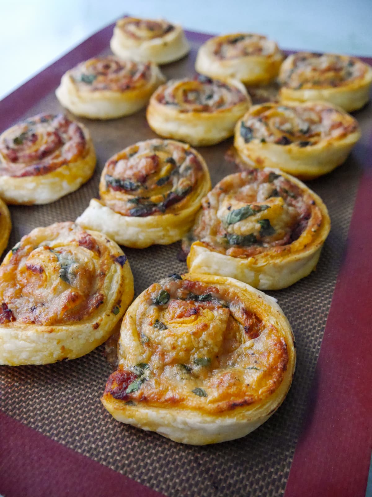 A lined baking sheet of freshly baked red pesto pinwheels.