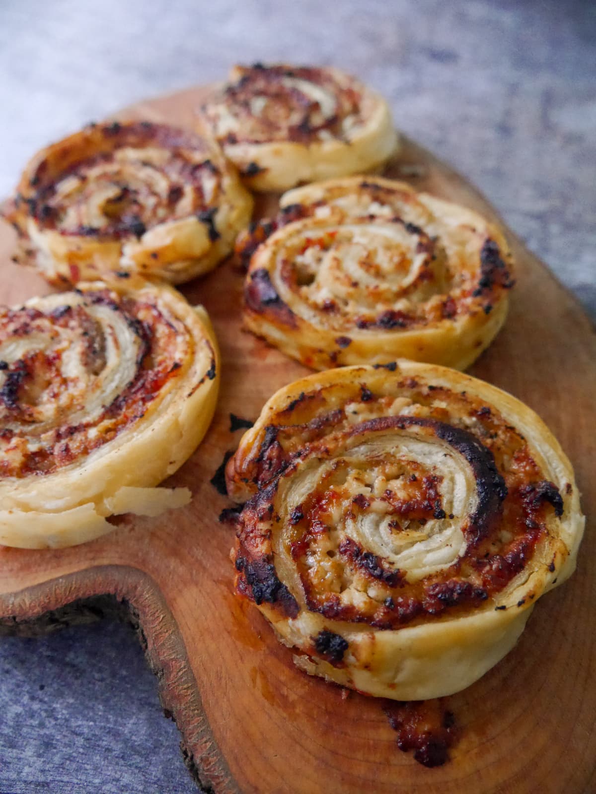 A wooden board topped with puff pastry sausage pinwheels.