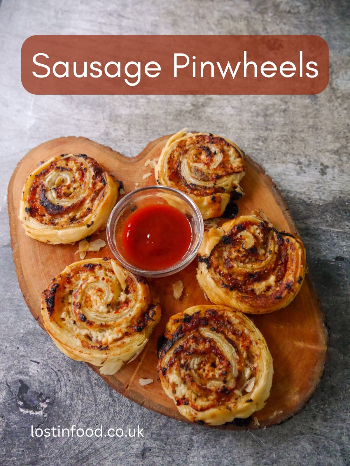Pinnable image with recipe title and a wooden board topped with puff pastry sausage pinwheels served with a bowl of tomato ketchup.