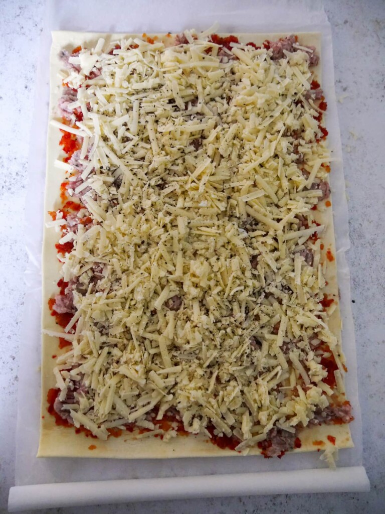A sheet of puff pastry topped with chilli jam, sausage meat and grated cheddar cheese.