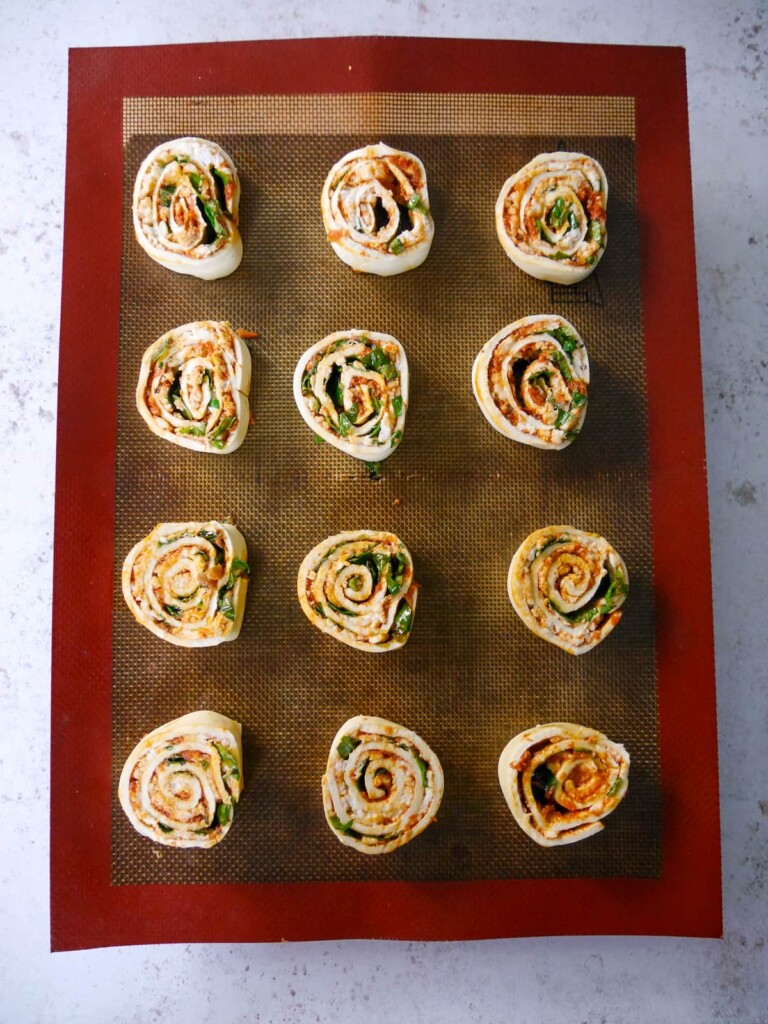 A line baking sheet of puff pastry pinwheels before being baked in oven.