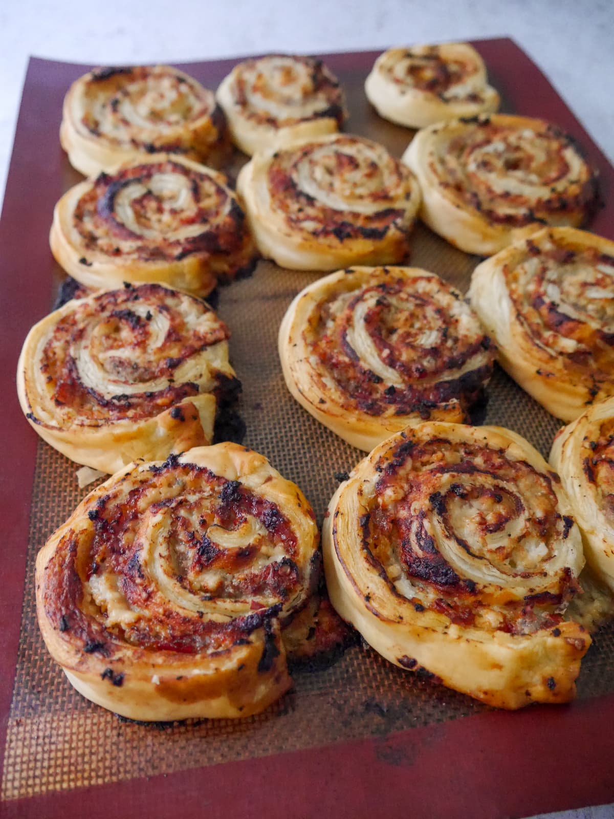 A lined baking sheet topped with cooked sausage pinwheels in puff pastry.