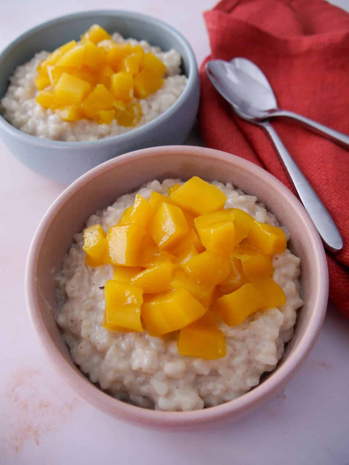 Two bowls of coconut rice pudding topped with chopped mango.