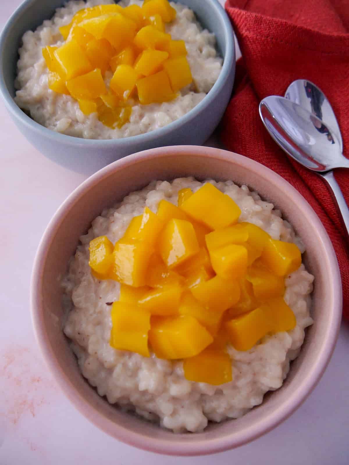 Two bowls of coconut rice pudding topped with chopped mango.