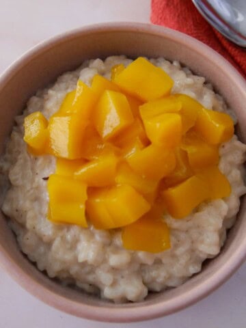 A bowl of coconut rice pudding topped with chopped mango.