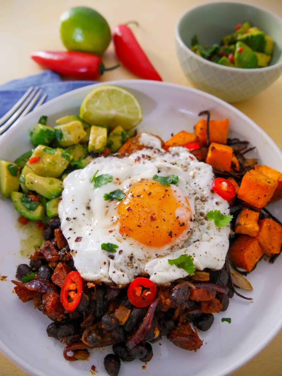 A bowl of cooked chorizo and black beans, roasted sweet potato and avocado salsa topped with a fried egg.