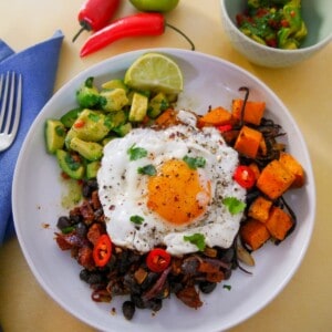 A bowl of cooked chorizo and black beans, roasted sweet potato and avocado salsa topped with a fried egg.