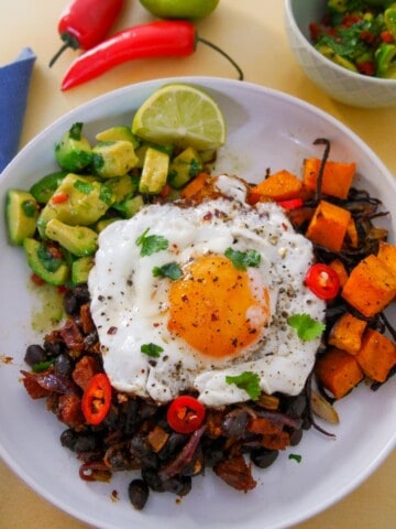 A bowl of cooked chorizo and black beans, roasted sweet potato and avocado salsa topped with a fried egg.