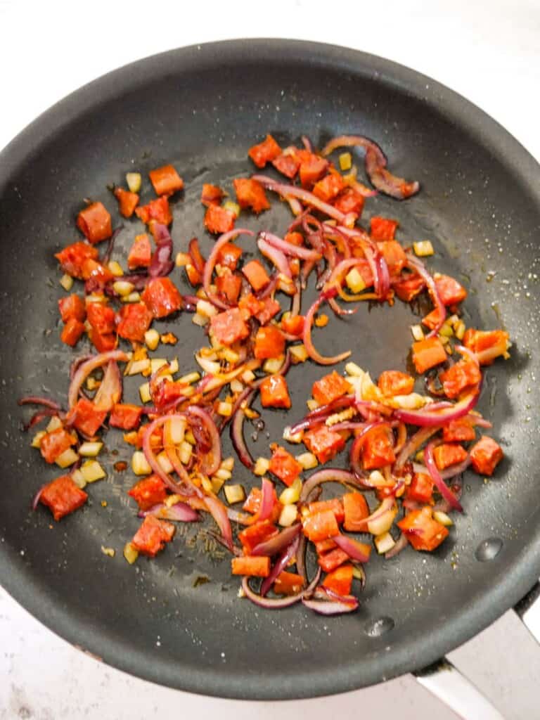 A saucepan of sauteed chorizo, red onion and garlic.
