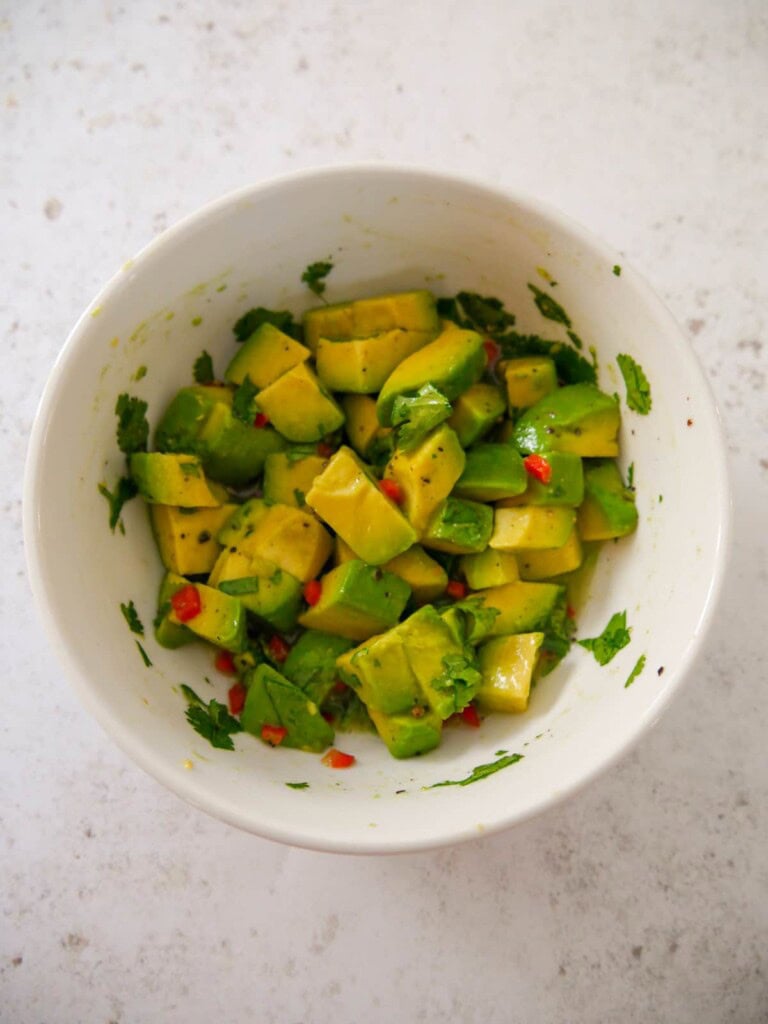 A bowl of chopped avocado combined with finely chopped red chilli, chopped coriander leaf, black pepper and lime juice.