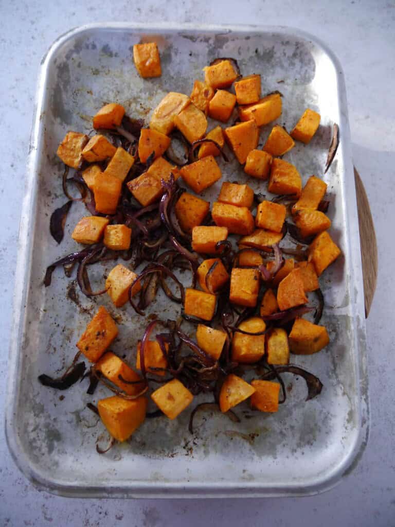 A baking sheet topped with roasted sweet potato cubes and sliced red onion.