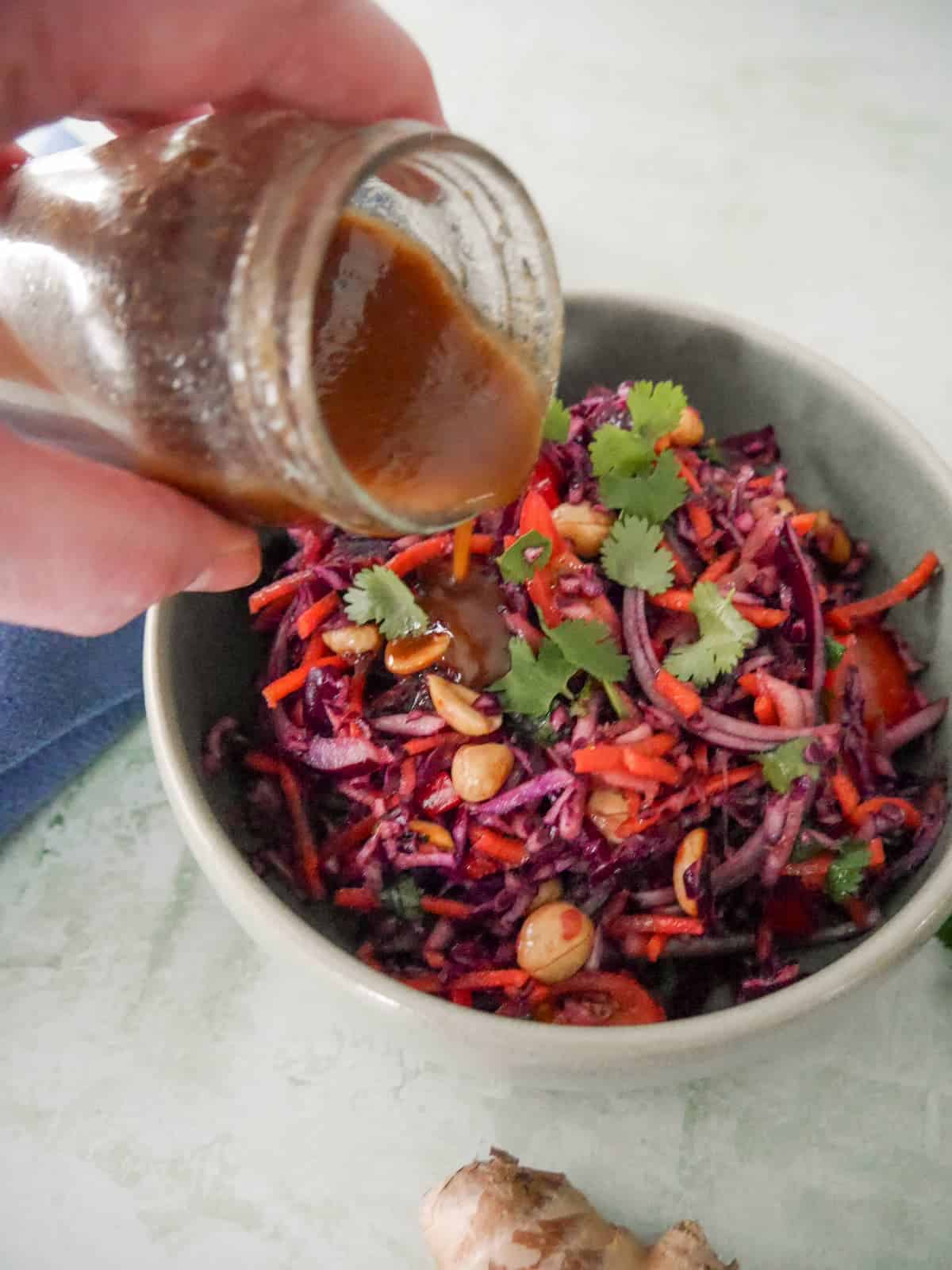 Soy and ginger dressing being poured over a bowl of roasted peanut and ginger slaw.