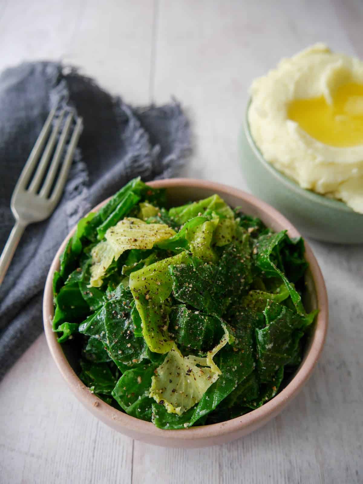 A bowl of buttered spring greens with a bowl creamy mashed potato set alongside.