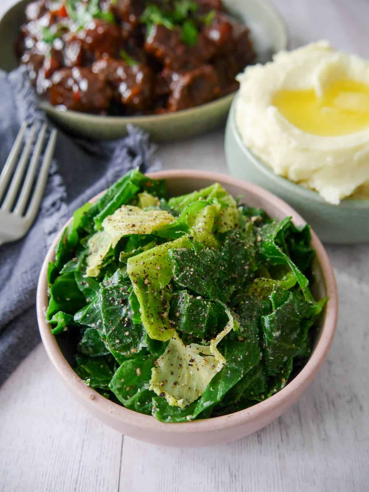 A bowl of buttered spring greens with a bowl paprika beef and a bowl of creamy mashed potato set alongside.