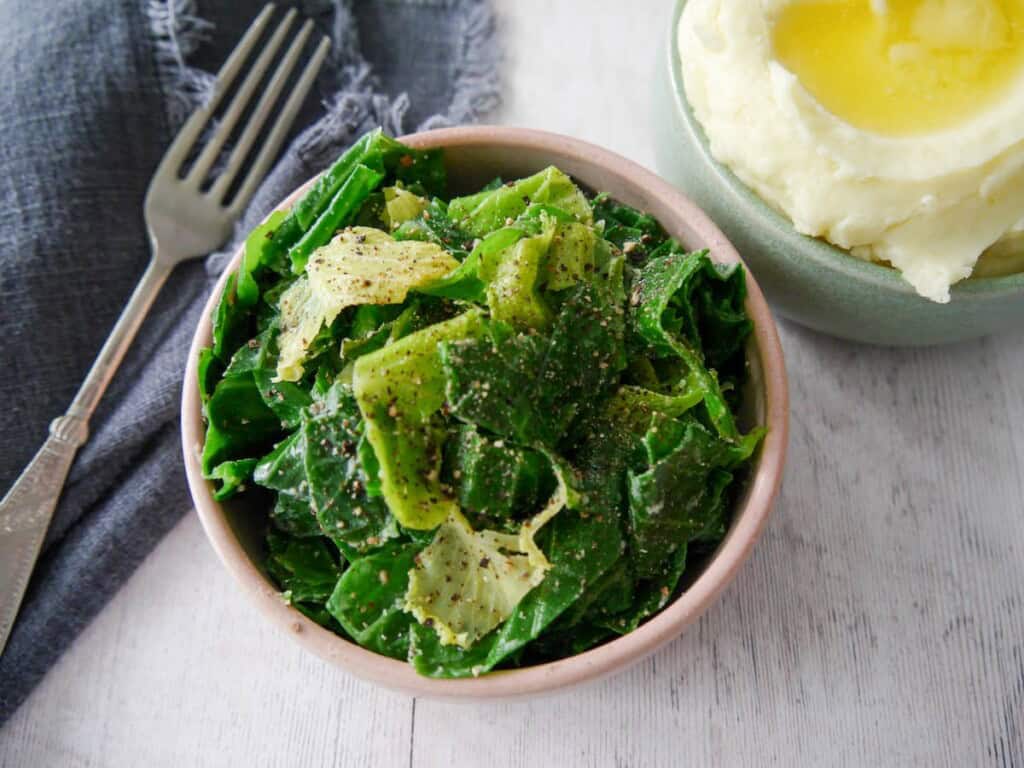 A bowl of buttered spring greens with a bowl creamy mashed potato set alongside.