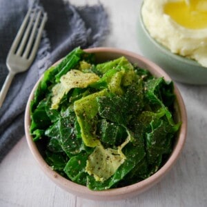 A bowl of buttered spring greens with a bowl creamy mashed potato set alongside.