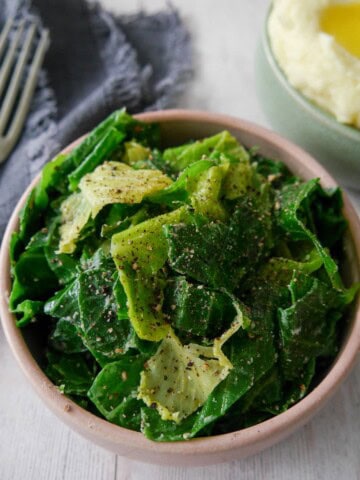A bowl of buttered spring greens with a bowl creamy mashed potato set alongside.