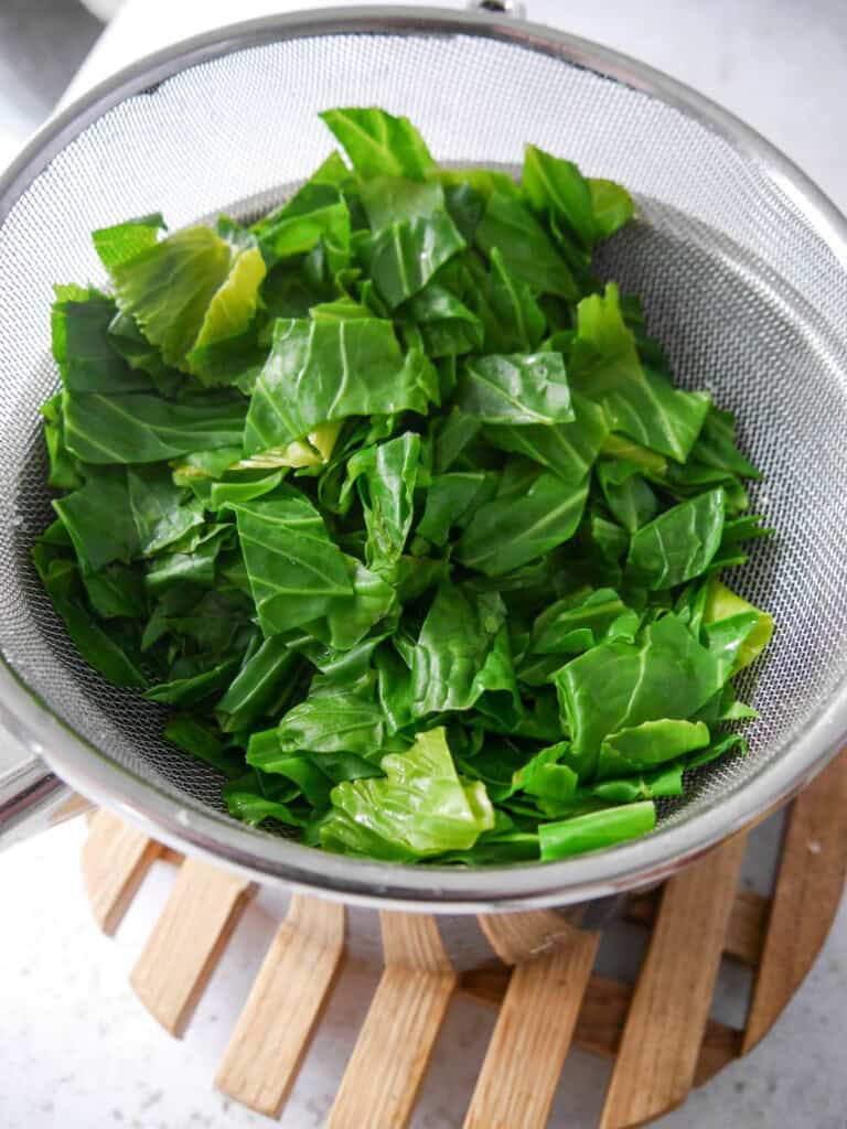 A sieve filled with cooked spring greens set over a saucepan to drain.