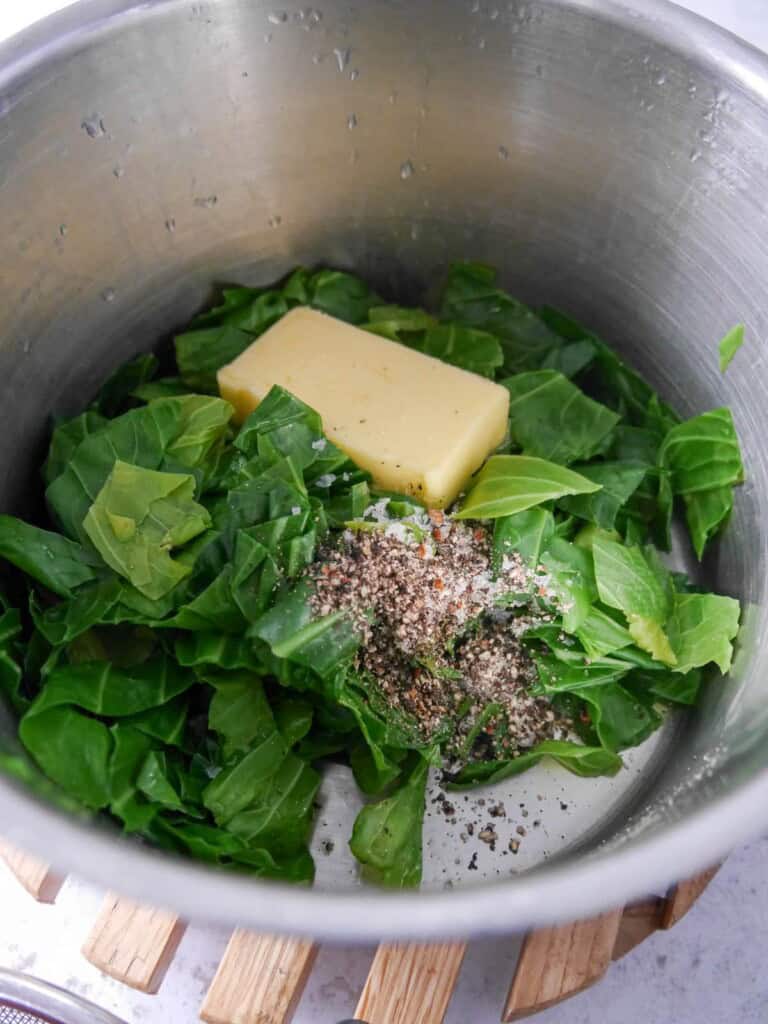 A saucepan of cooked spring greens with added butter, sea salt and black pepper.