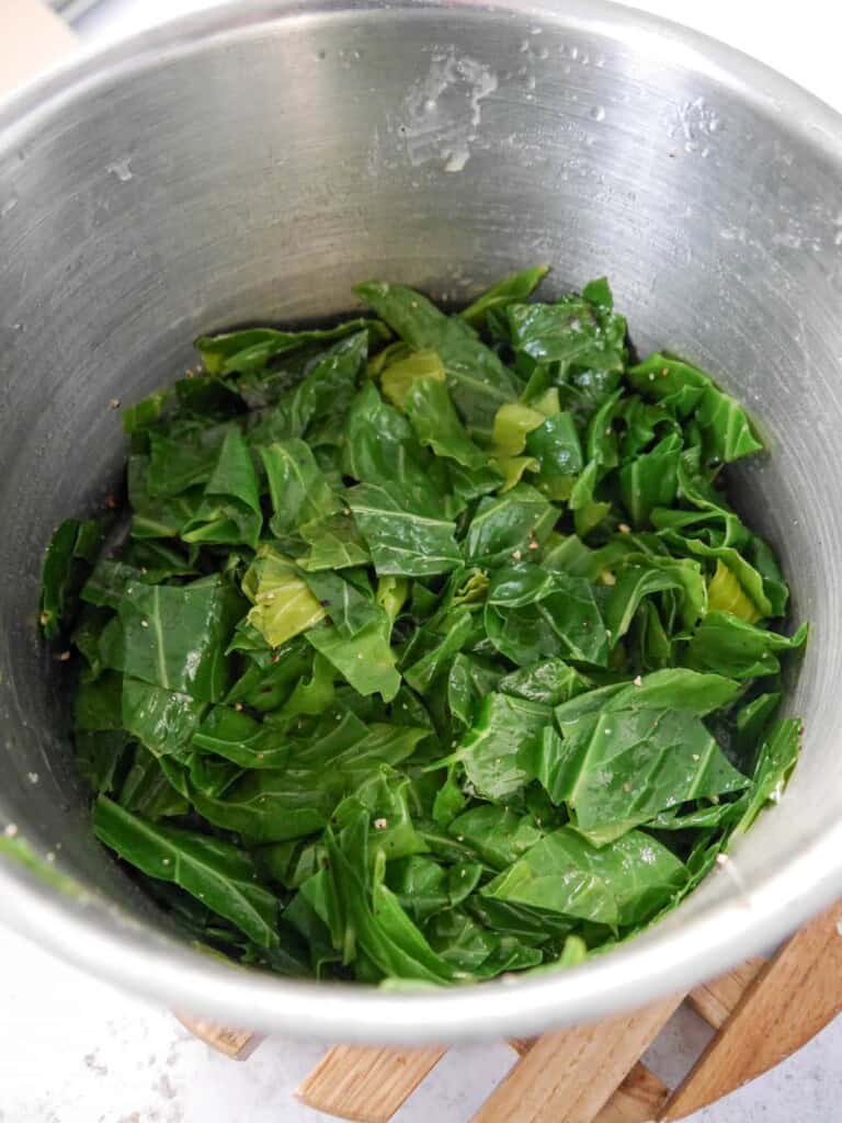 A saucepan of cooked spring greens with added butter and black pepper.