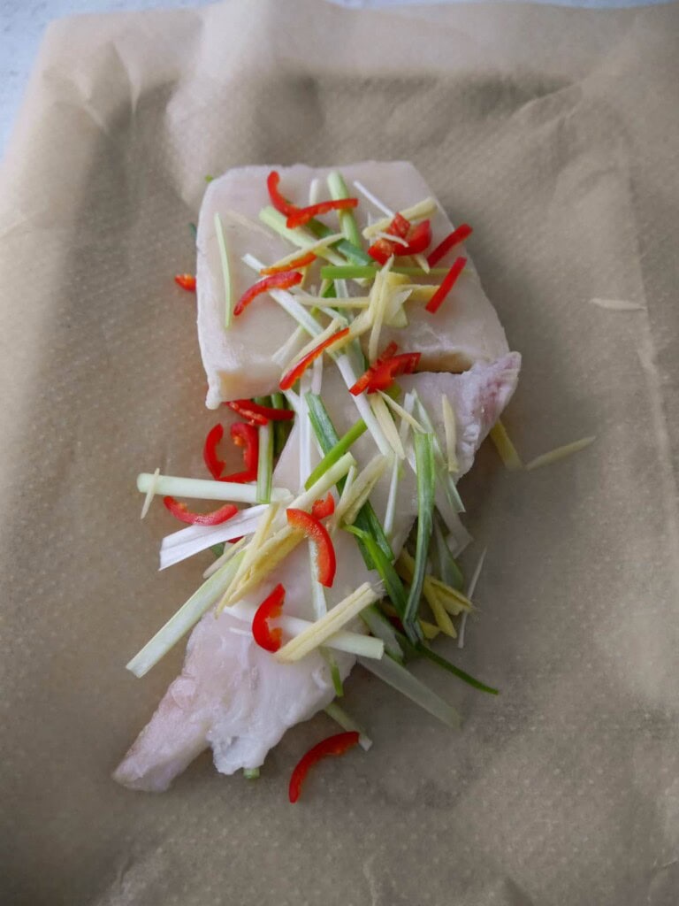 Raw white fish fillets with sliced red chilli, root ginger and spring onions set underneath the fish and sprinkled over the top.