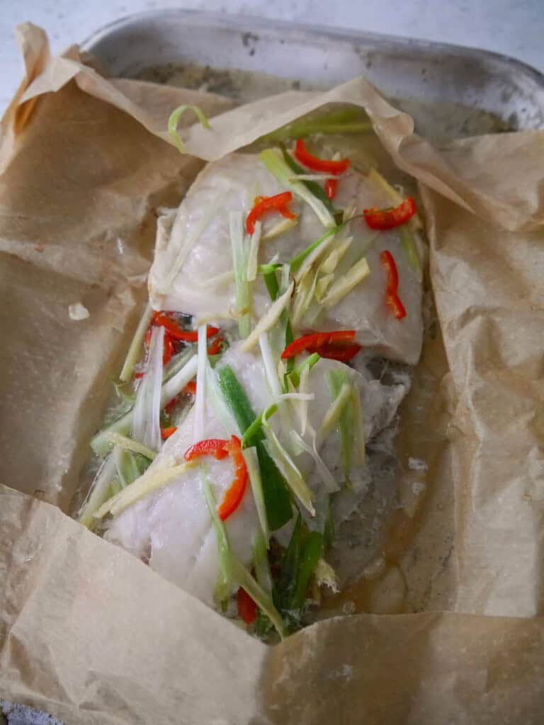 Steamed fish fillets with sliced ginger, spring onion and chilli in an opened parchment paper parcel.