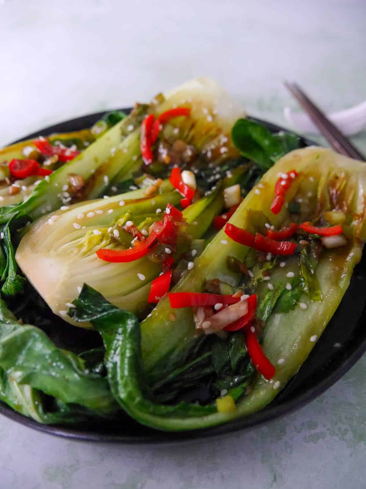 A plate of Chinese stir fry pak choi with garlic, red chillies and spring onion, garnished with sesame seeds.