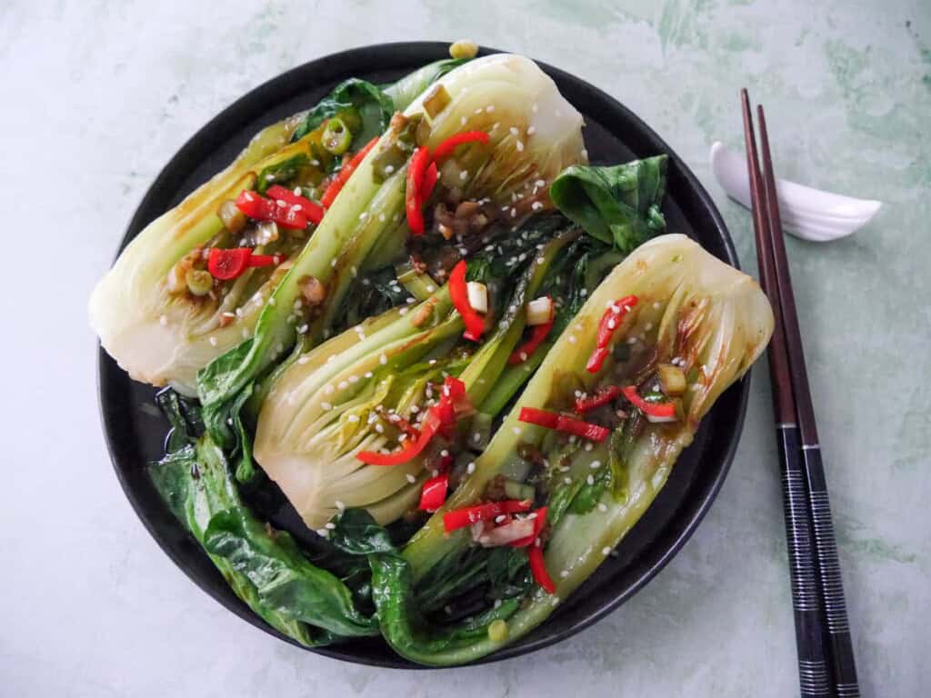 A plate of Chinese stir fry pak choi with garlic, red chillies and spring onion, garnished with sesame seeds.