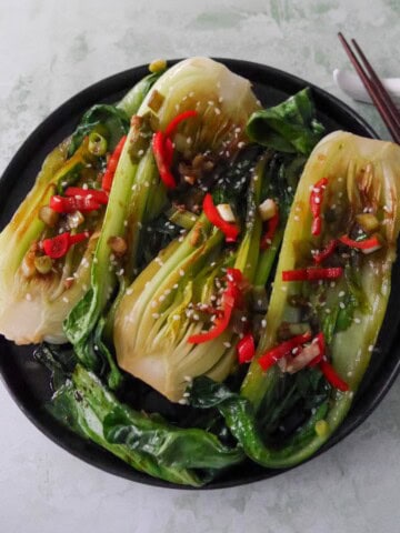 A plate of Chinese stir fry pak choi with garlic, red chillies and spring onion, garnished with sesame seeds.