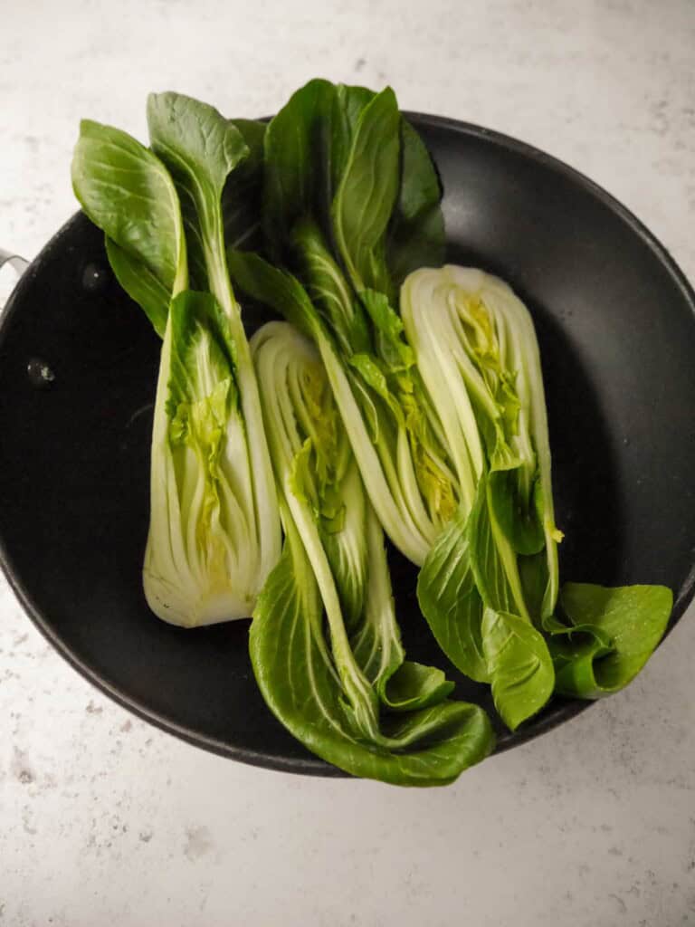 A wok with raw halves of pak choi.