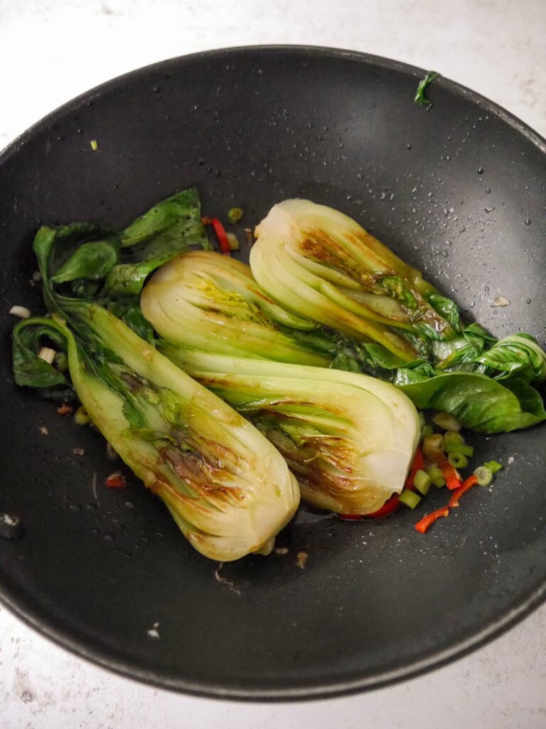 A wok of stir fry pak choi with sliced red chilli, spring onion and crushed garlic.